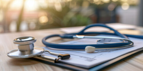 Close up of a stethoscope on medical bills with a laptop and calculator in the background, highlighting healthcare costs.