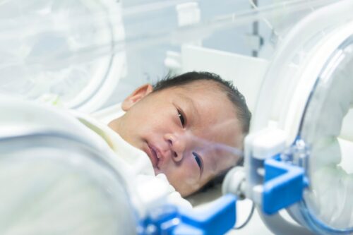 Newborn in hospital incubator receiving neonatal care after a difficult delivery